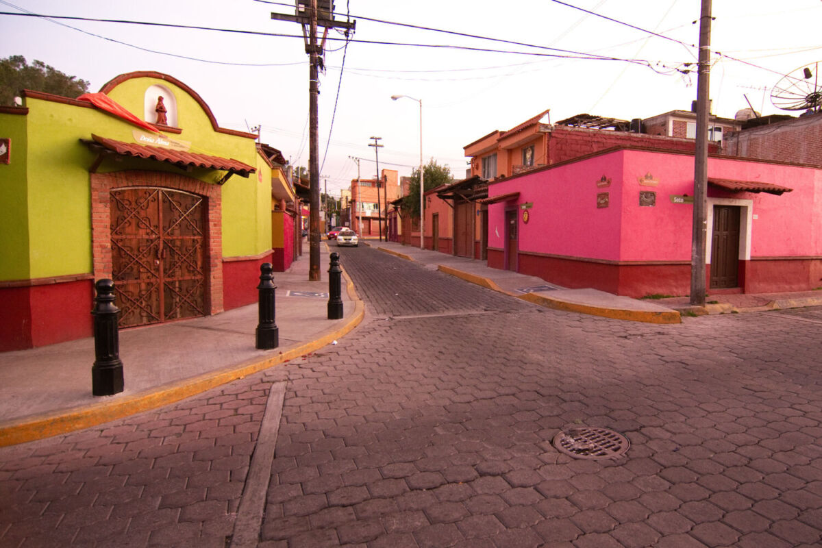 Calle adoquinada en Metepec con fachadas pintadas de amarillo y rosa, arquitectura colonial del Pueblo Mágico más pequeño de México
