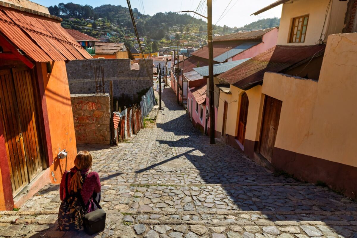 Calle empedrada en pendiente de Real del Monte con casas de techo de lámina y bosque de pinos al fondo
