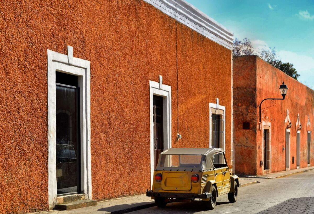 Fachadas coloniales color naranja en una calle tranquila de Valladolid, Yucatán, con un auto clásico estacionado