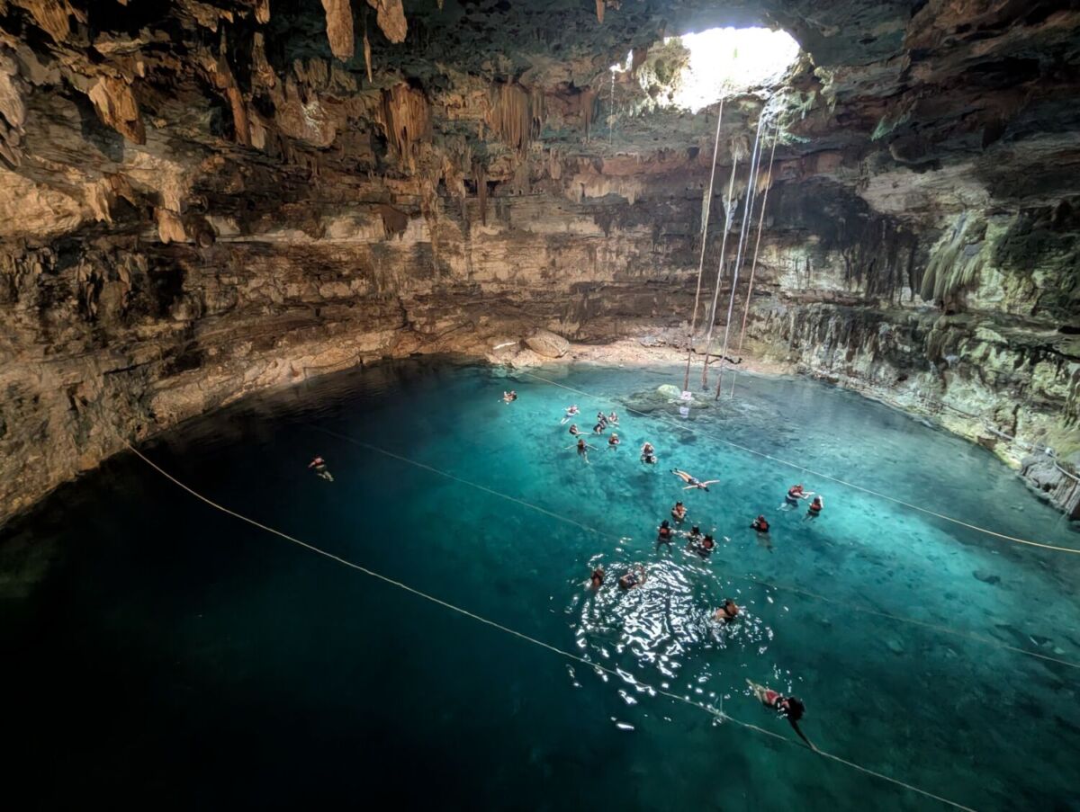 Interior del cenote Zací en Valladolid, con agua azul turquesa y visitantes nadando