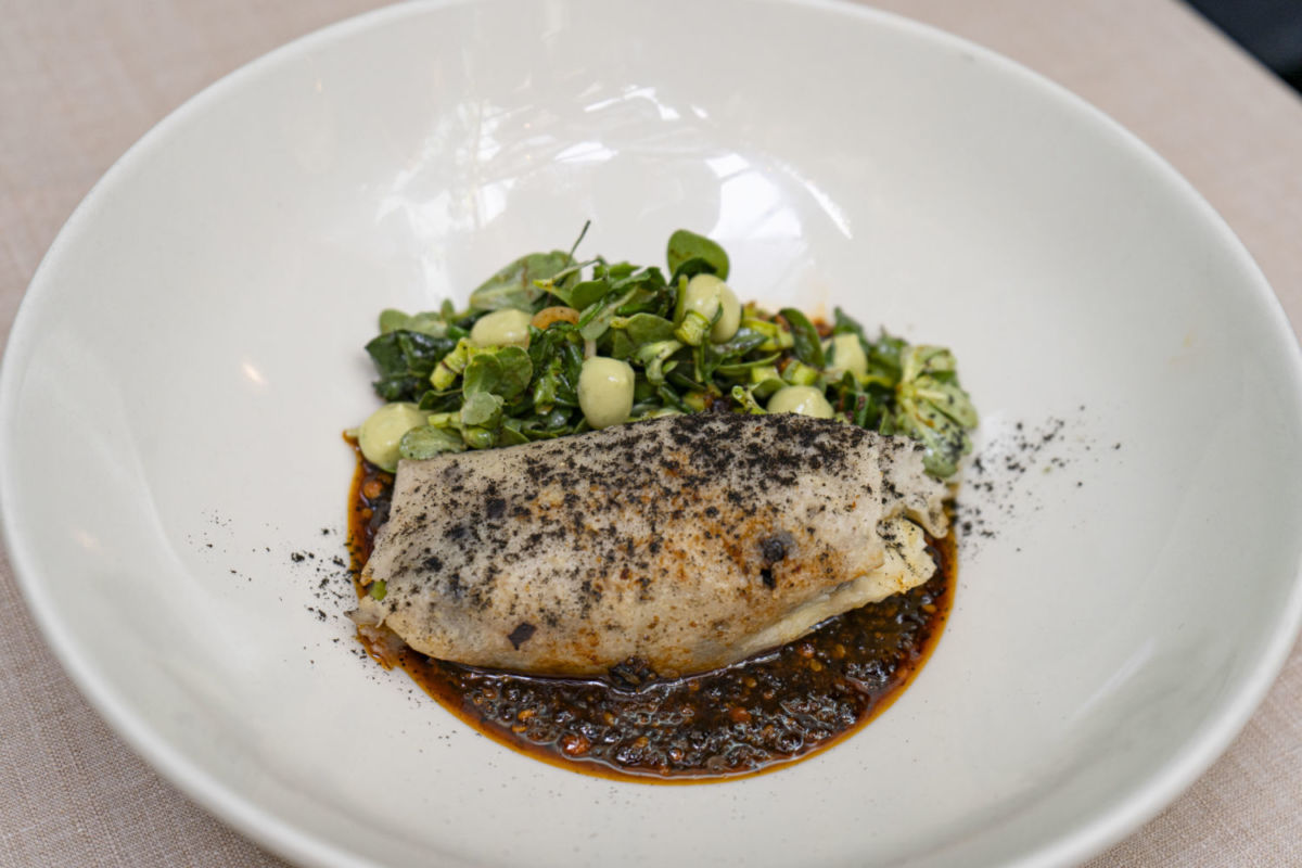 Tamal de frijol con quelites, servido sobre una salsa macha