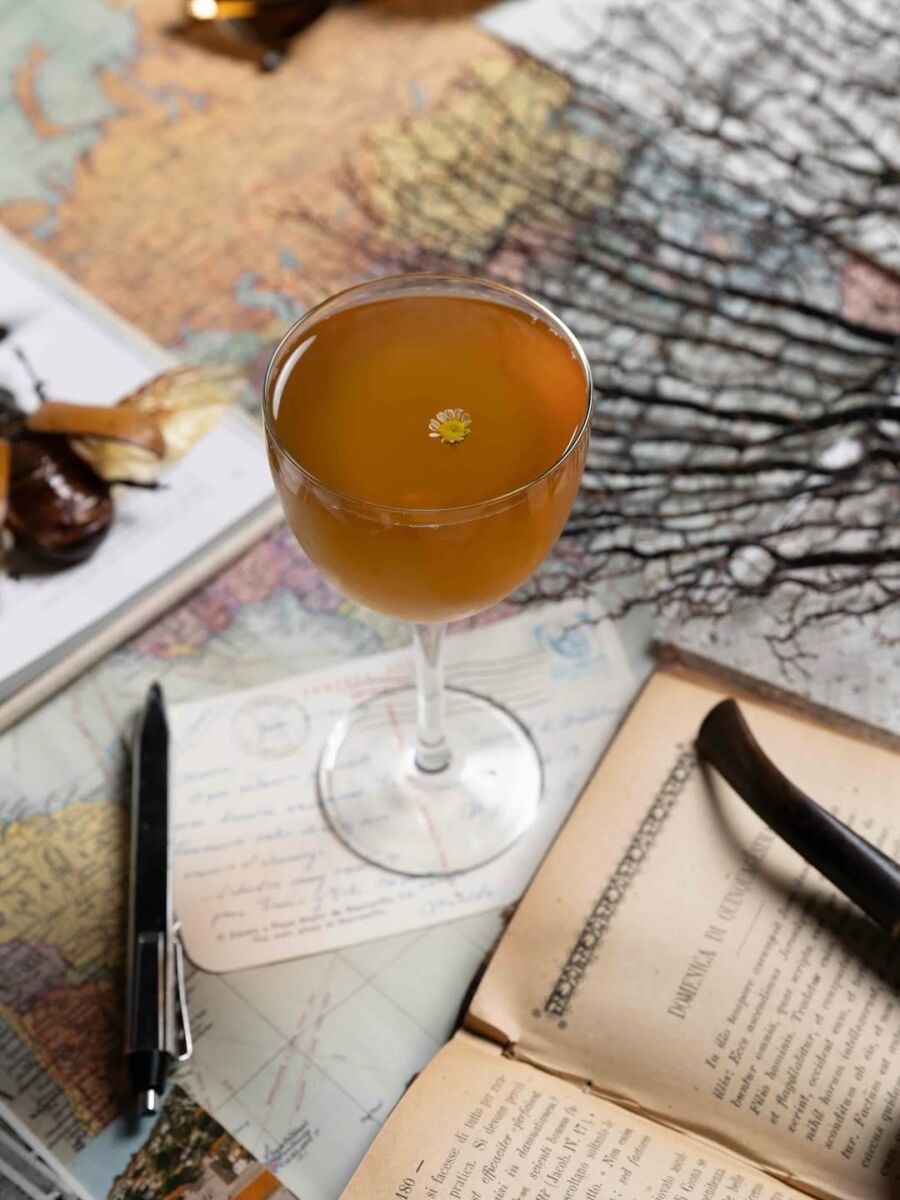 copa de cristal con un coctel color ámbar decorado con una flor