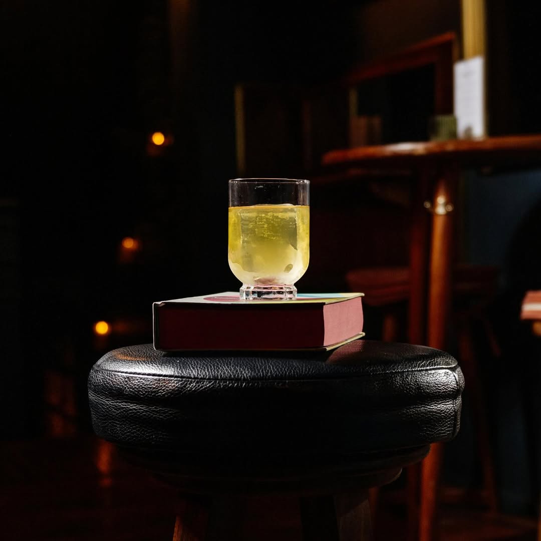 vaso de cristal con un líquido amarillo intenso, colocado sobre un libro y una silla
