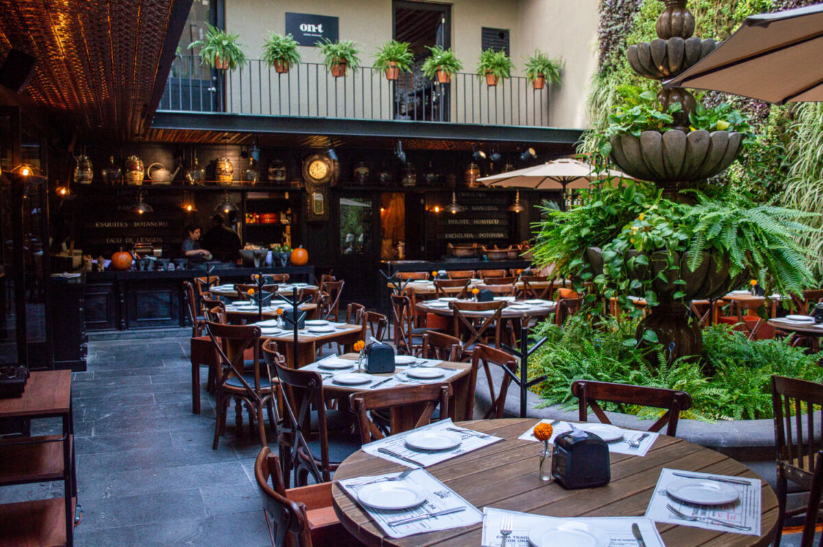 patio interior con mesas redondas y una fuente con plantas