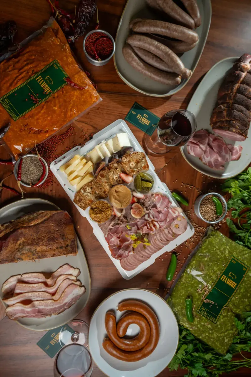 mesa puesta con una tabla de charcuteria con quesos, salchichas, salami y copas de vino