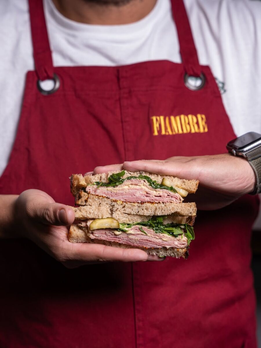 persona sosteniendo dos sándwiches de jamón con queso y espinacas