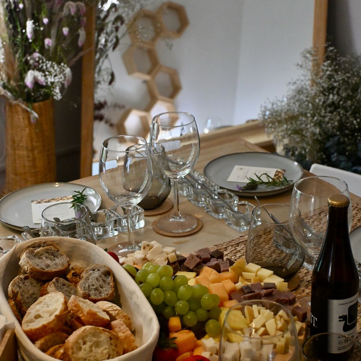 toma cerrada de una mesa puesta con copas de vidrio una canasta de pan, quesos y fruta