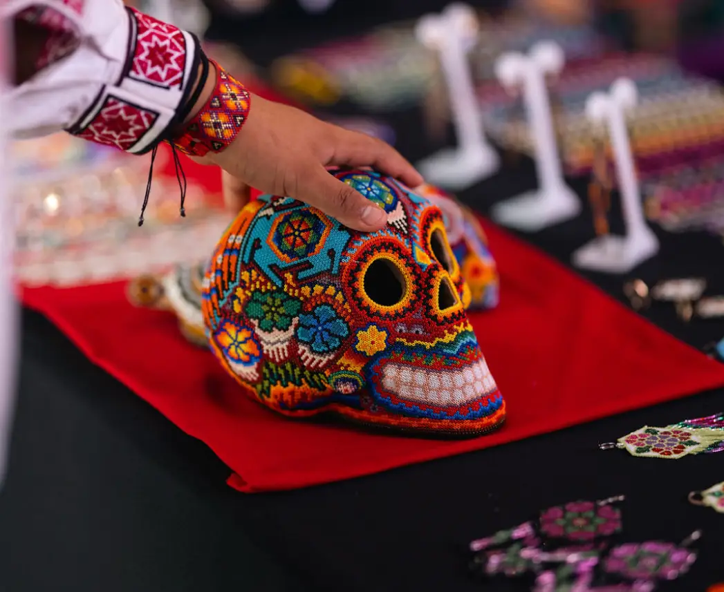 mano tocando un cráneo artesanal cubierto de chaquiras de colores
