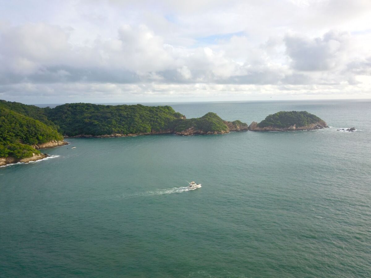 panoramica del mar con una lancha navegando y una gran isla con vegetación tropical al fondo