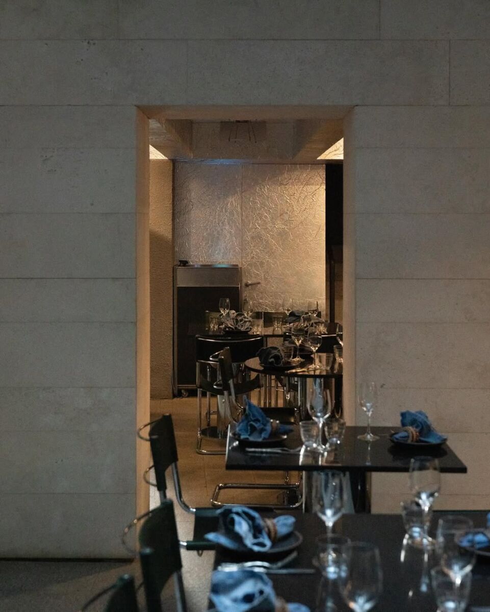 restaurante de arquitectura minimalista con mesas cuadradas alineadas, con copas de cristal y servilletas de mezclilla