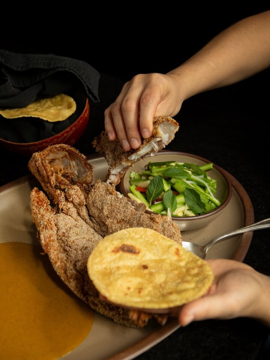 manos preparando pescado frito con un plato de verduras y una tortilla