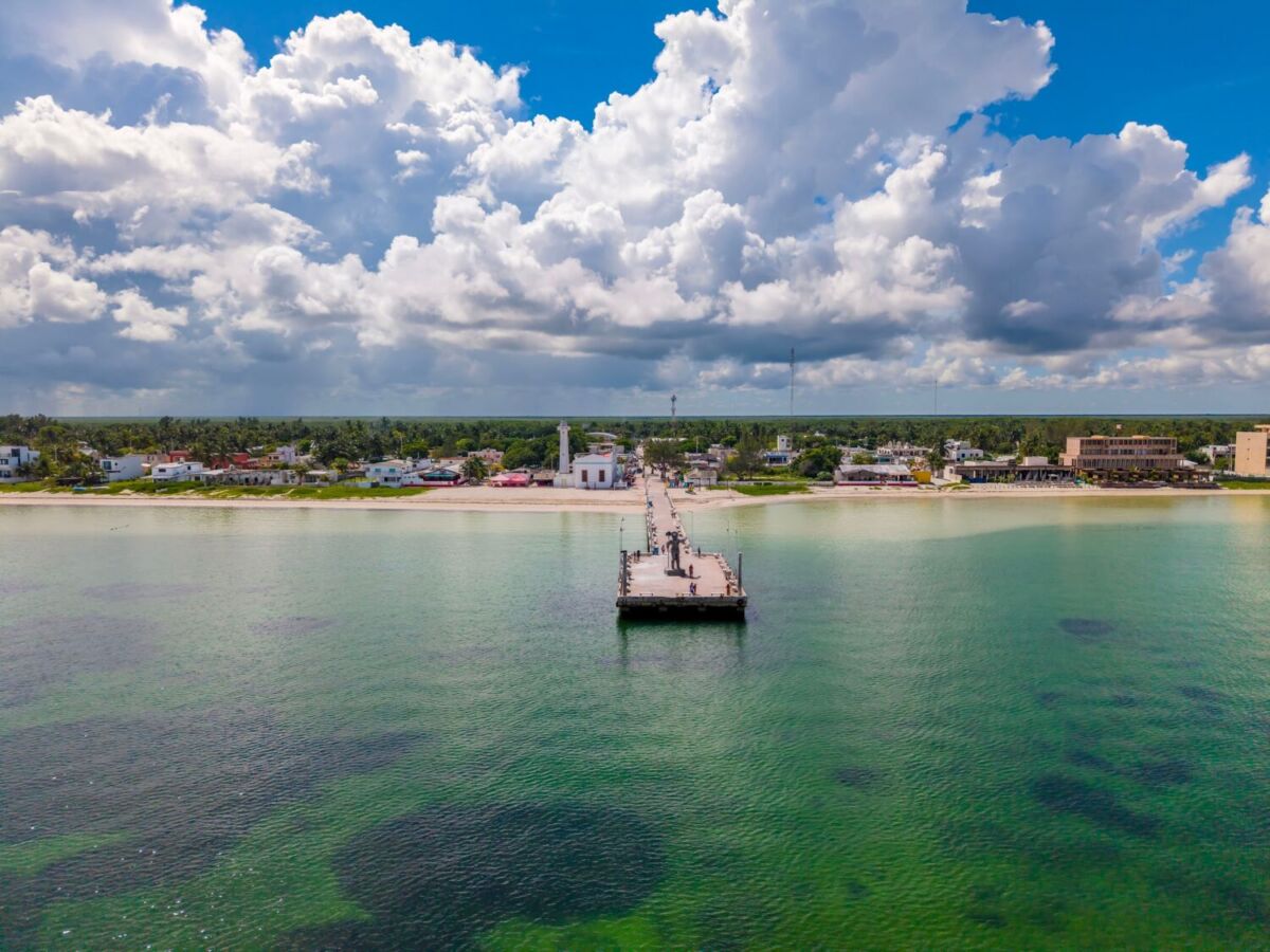 panoramica vista desde el mar turquesa de una playa con un muelle al centro y el cielo azul con nubes