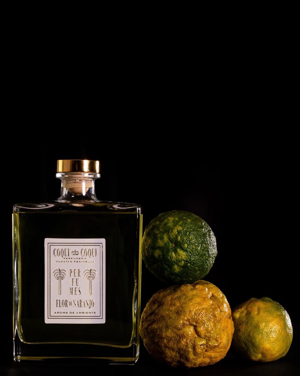 botella de cristal cuadrada con etiqueta blanca junto a tres naranjas con cáscaras rugosas