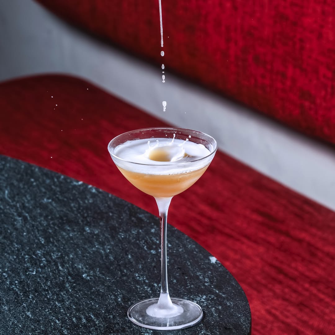coctel color coral en una copa de cristal elegante sobre una mesa de granito