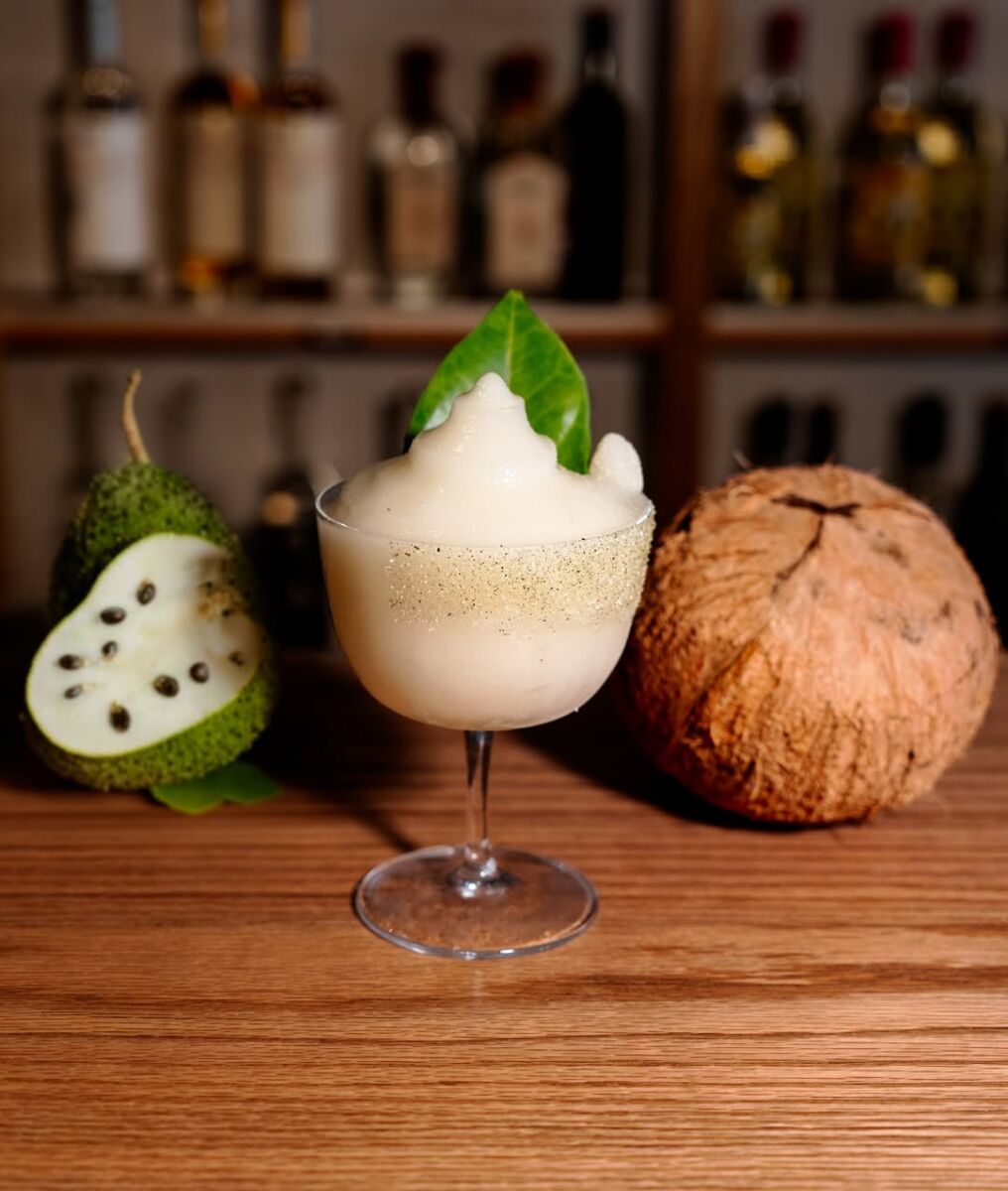 margarita frozen decorada con una hoja, colocada entre una guanábana partida por la mitad y un coco