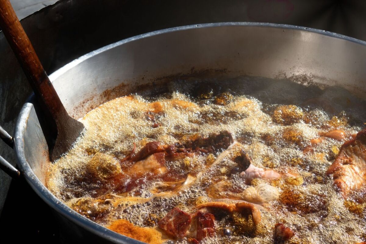Cuchara enorme de madera levantando chicharrón y carnitas recién salidas del cazo de cobre en Carnitas Carmelo, Quiroga.