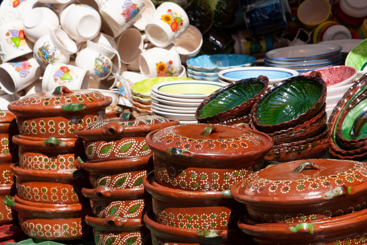 Puestos de artesanías en el mercado de Quiroga, Michoacán mostrando cazuelas de barro decoradas con puntos blancos y verdes apiladas.