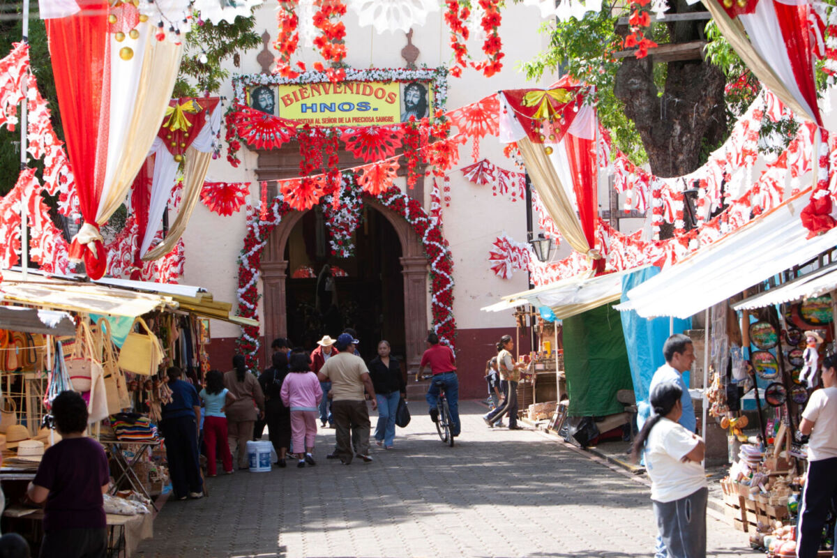 Calle empedrada del mercado de Quiroga decorada con papel picado rojo y blanco colgando entre los puestos de artesanías. 