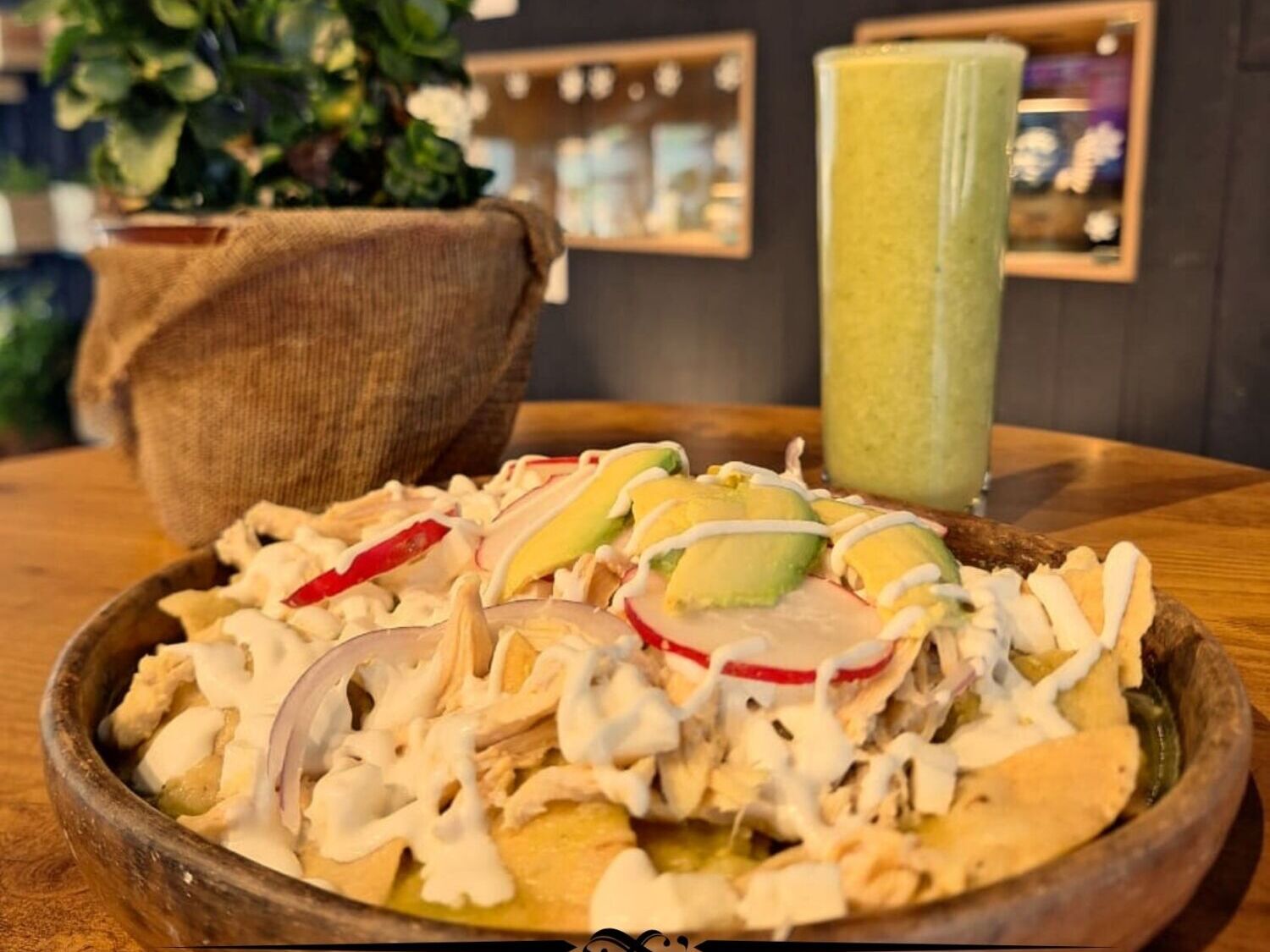 plato de chilaquiles verdes con crema, queso y aguacate, con jugo verde detrás