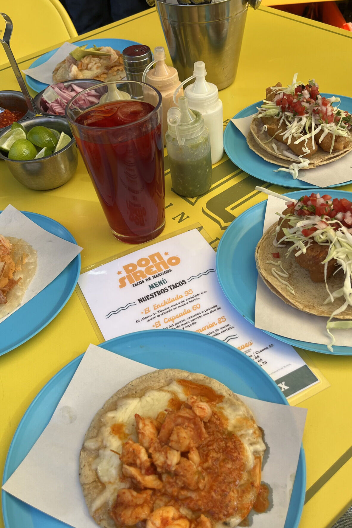 mesa amarilla de lámina con tacos de pescado y camarón en platos de plástico