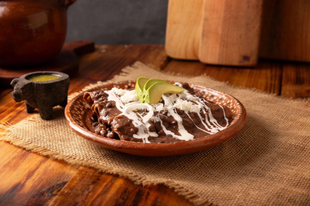 enfrijoladas con crema y aguacate servidas en un plato de barro sobre una mesa de madera
