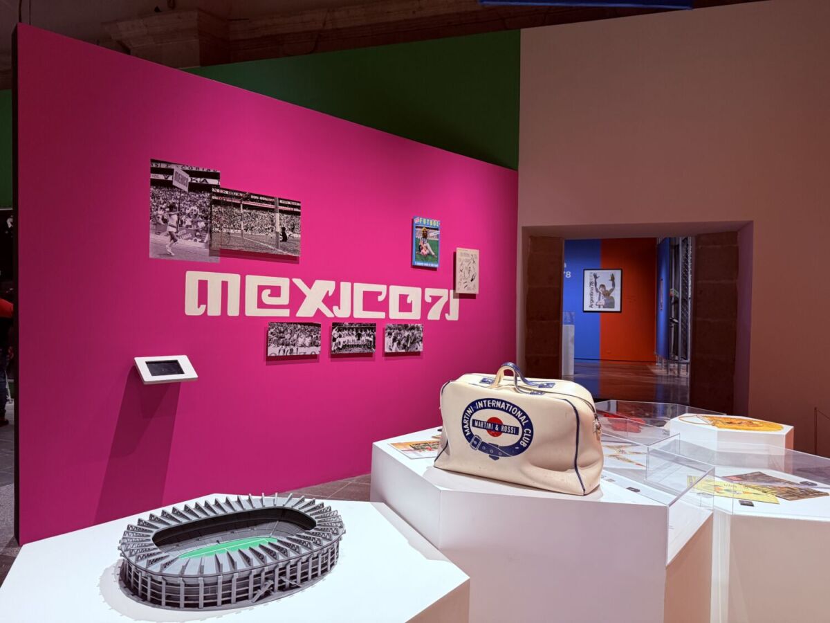 muro rosa con la leyenda 'méxico 71', una maqueta de un estadio y un maletín blanco