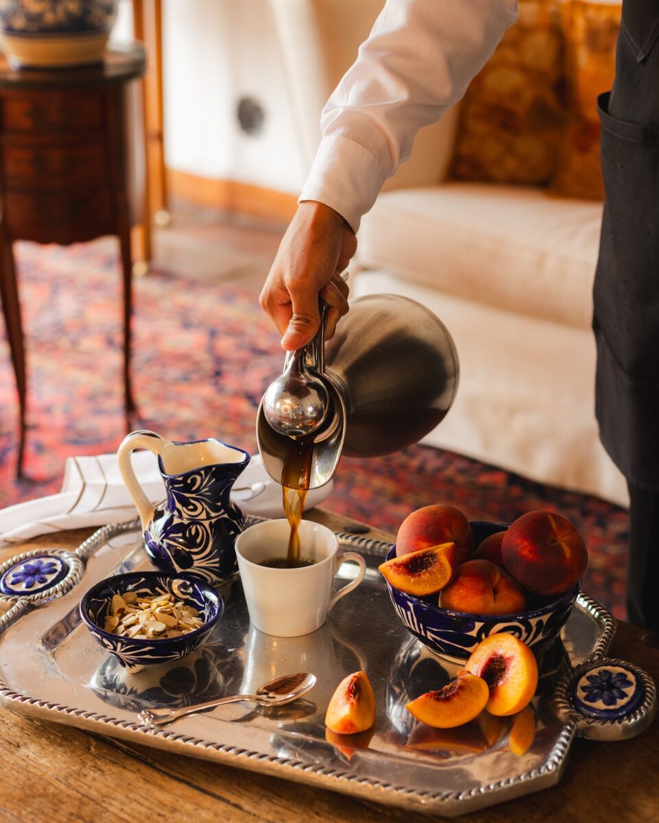 mesero sirviendo café en una taza sobre una charola con duraznos y almendras fileteadas