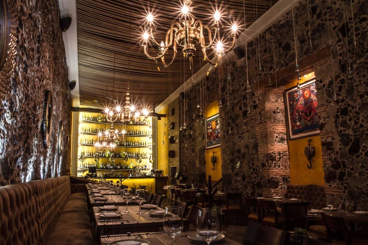 Interior de Limosneros restaurante con muros de piedra volcánica candelabros y barra iluminada en el Centro Histórico CDMX.