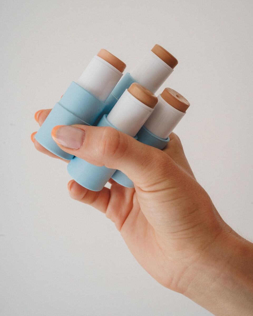 mano sosteniendo cuatro barras de maquillaje con empaques azul claro