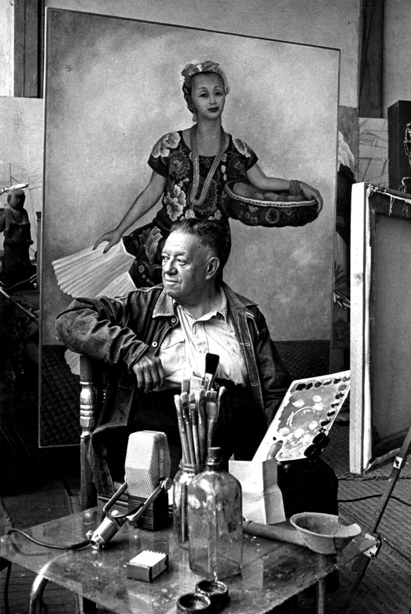 fotografía en blanco y negro de diego rivera anciano pintando con un retrato de dolores olmedo detrás