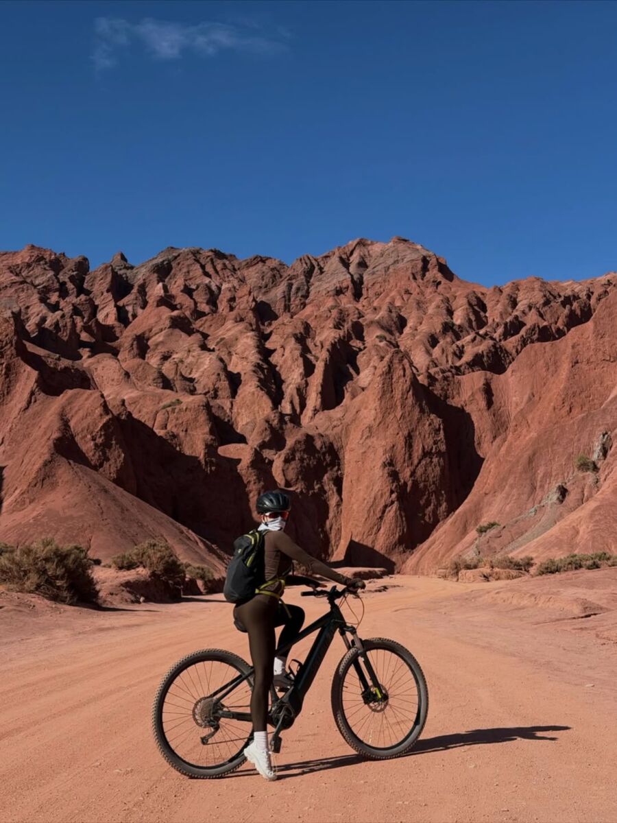 mujer posando en bicicleta frente a formaciones rocosas en el desierto