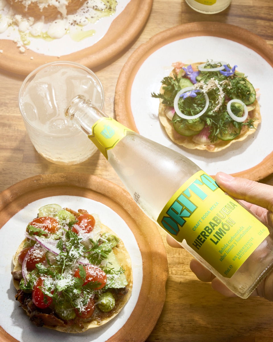 mano sosteniendo una botella de orita sobre dos platos de comida mexicana