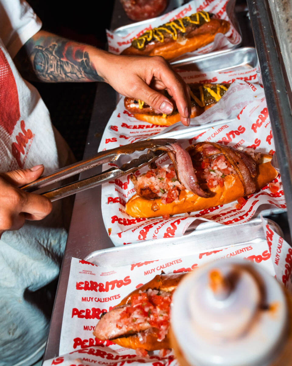 persona preparando un hot dog con tocino