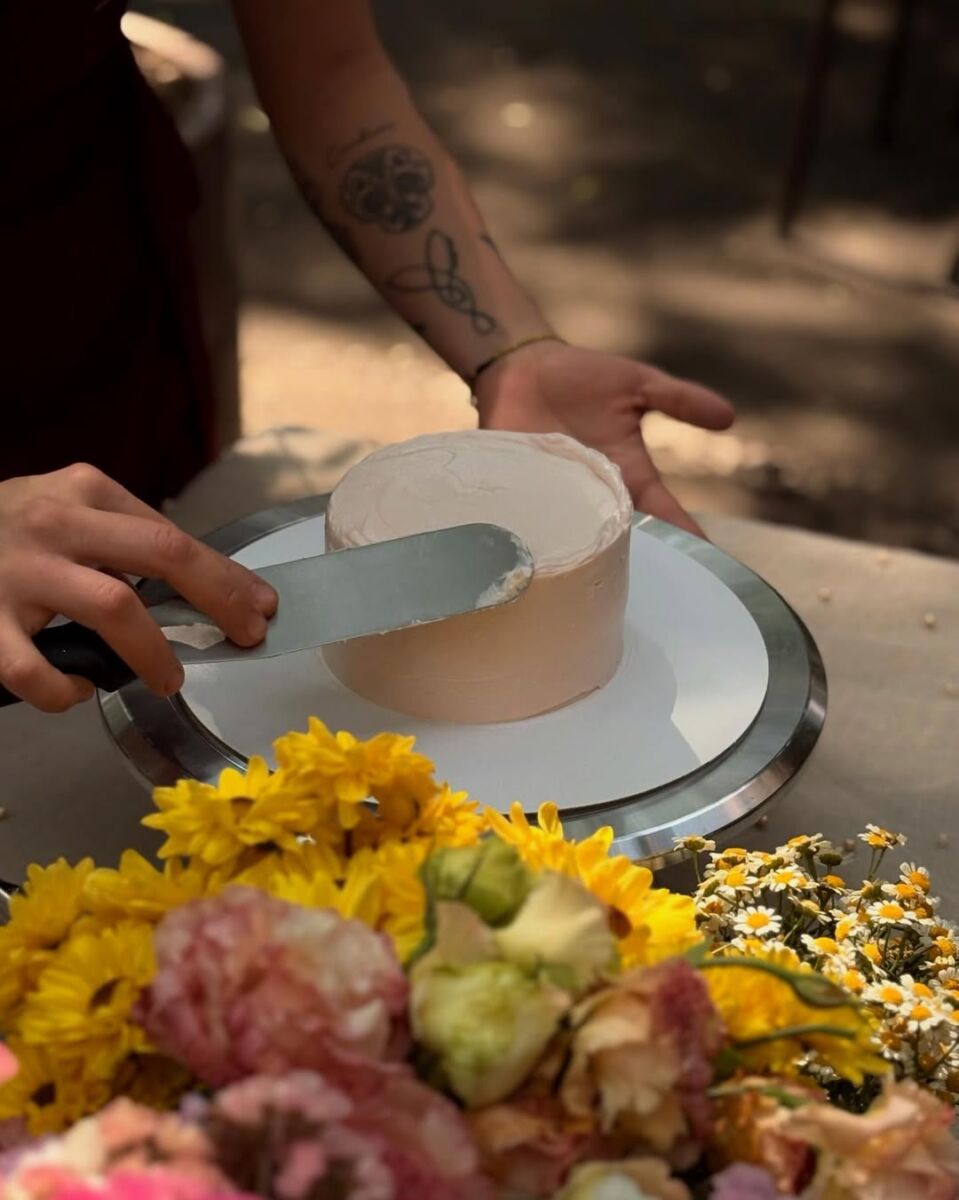 manos decorandoselas un pastel con una espátula y betún rosa pálido