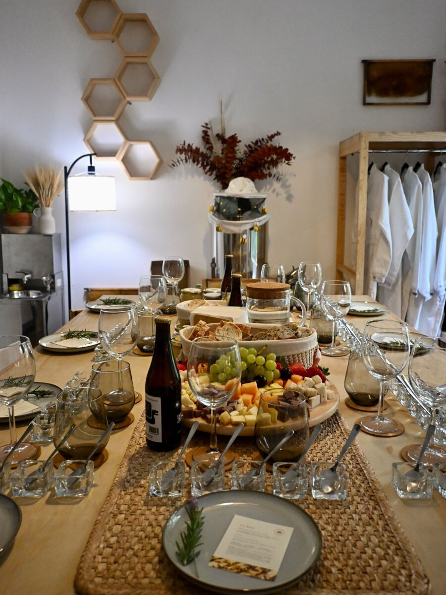 mesa puesta con copas de cristal, botellas de hidromiel, tablas de quesos, fruta y un panal de miel