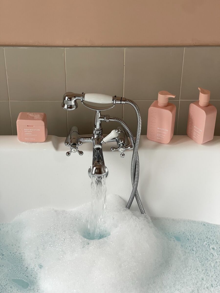 close up de una bañera abeirta con burbujas y productos de baño color rosa en la orilla