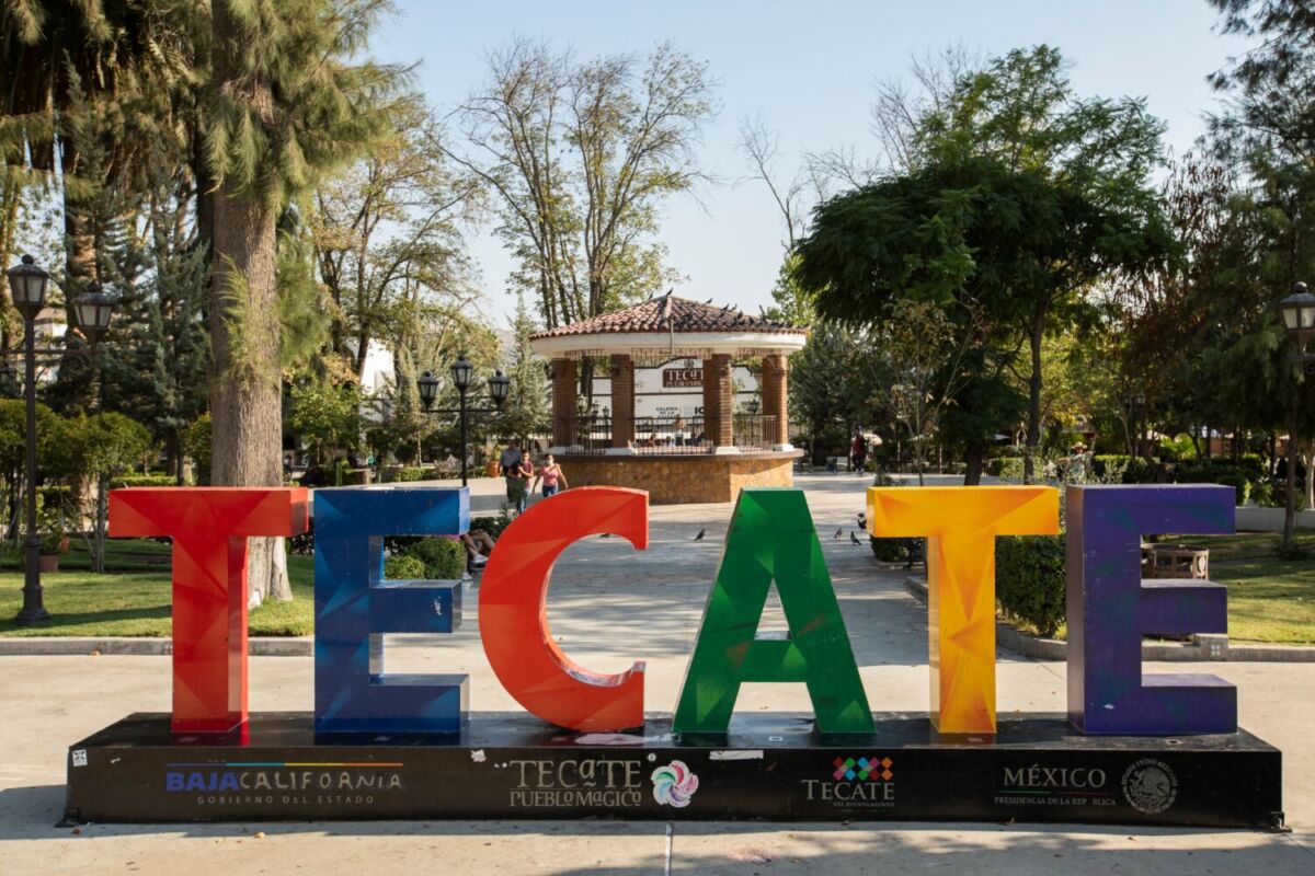 letras de colores de 'TECATE' con un kiosco y árboles atrás