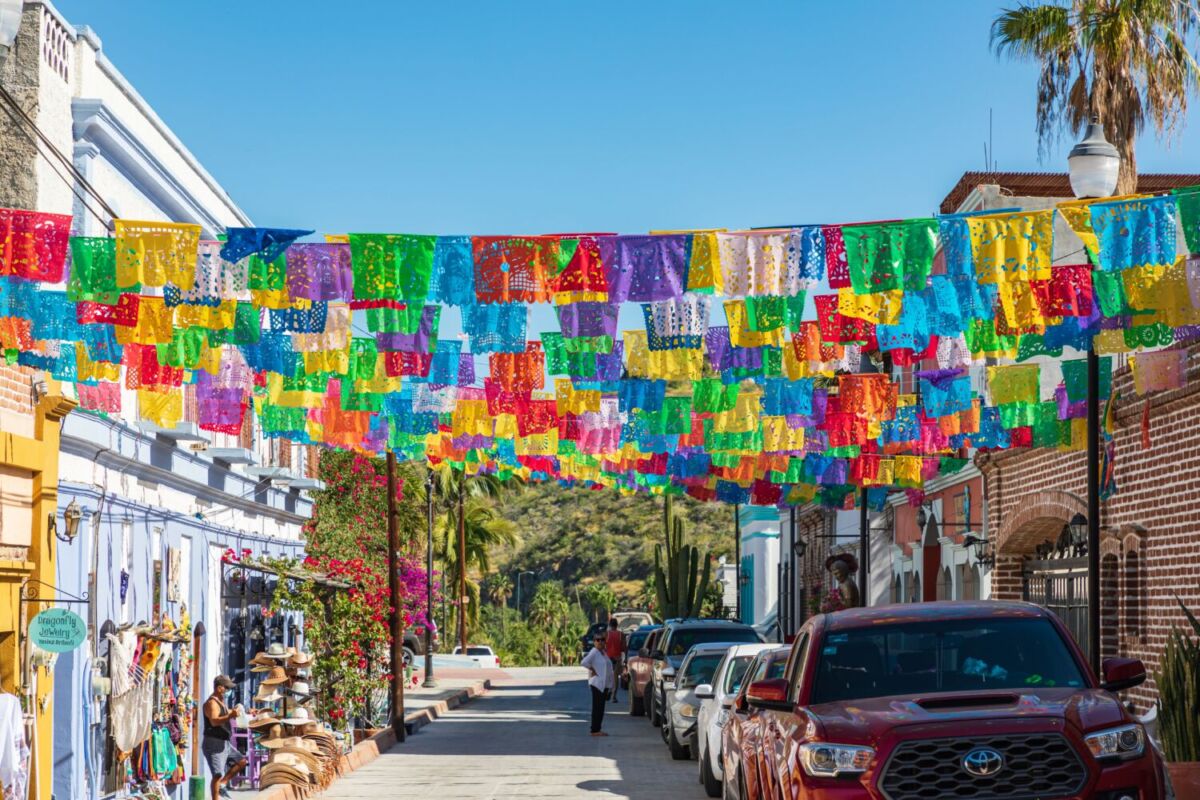Calle principal de Todos Santos con papel picado colorido, palmeras y montañas al fondo, Baja California Sur