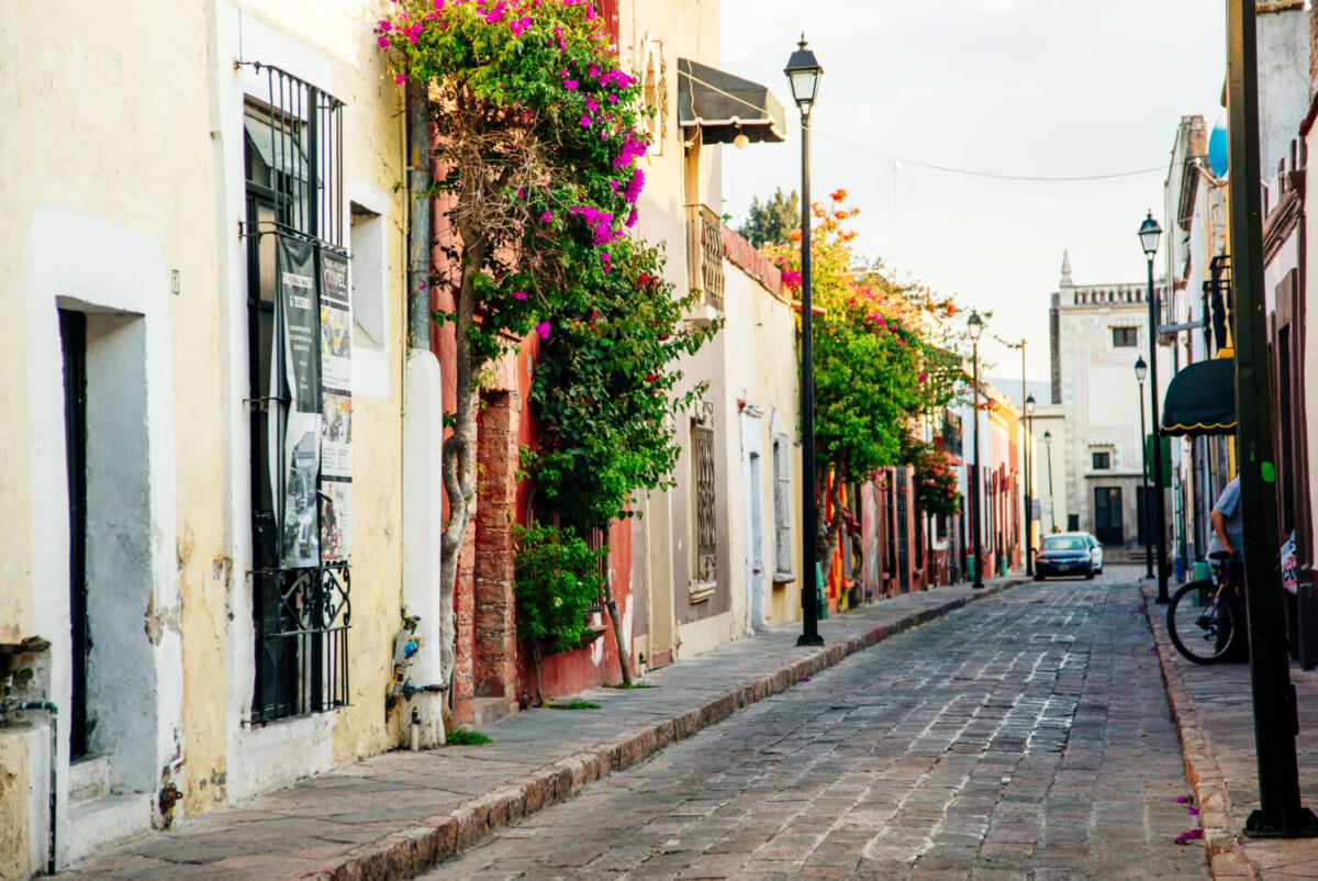 alle empedrada de Xochitepec con fachadas coloniales en tonos amarillo, naranja y rosa, puertas de madera antigua y bugambilias rojas colgando de arco de cantera bajo luz dorada del atardecer