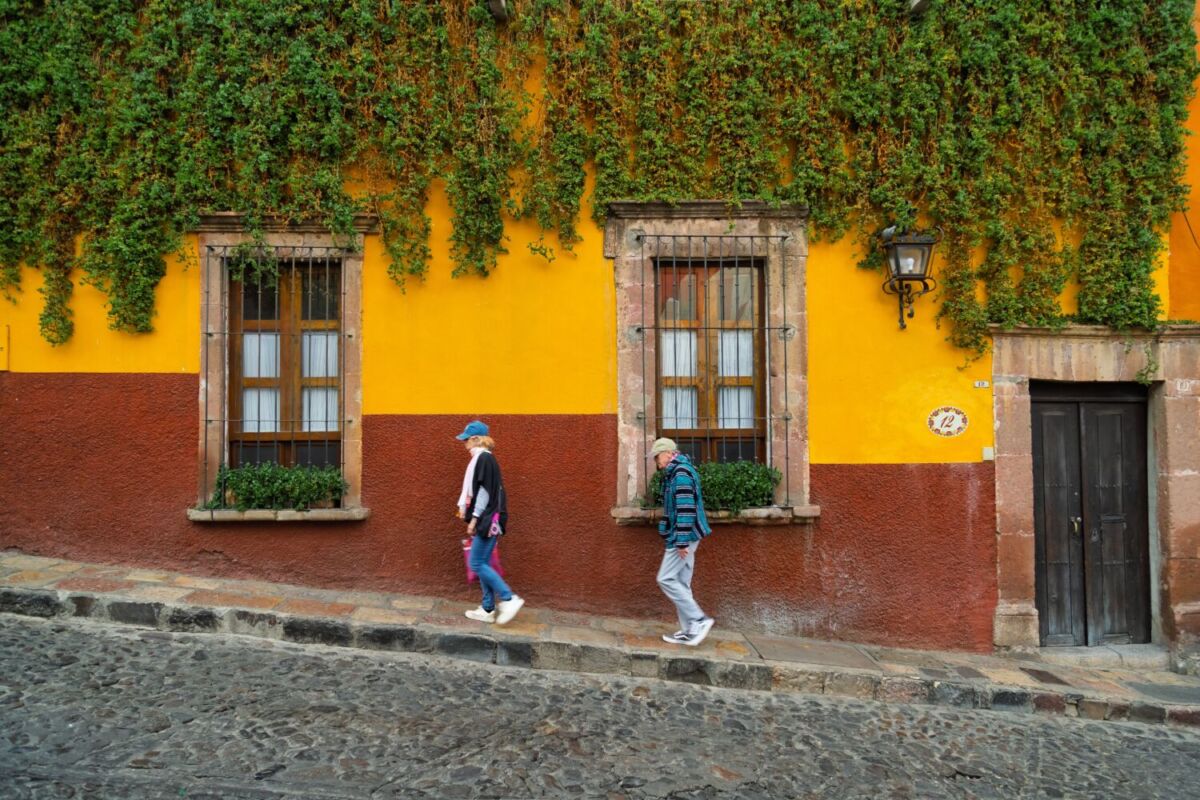 dos personas caminando por una calle empedrada con casona colorida 