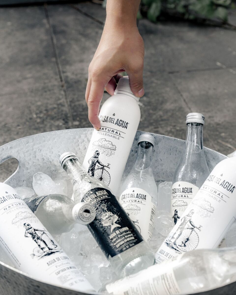 mano sacando una botella de agua de una cubeta con hielo y más botellas