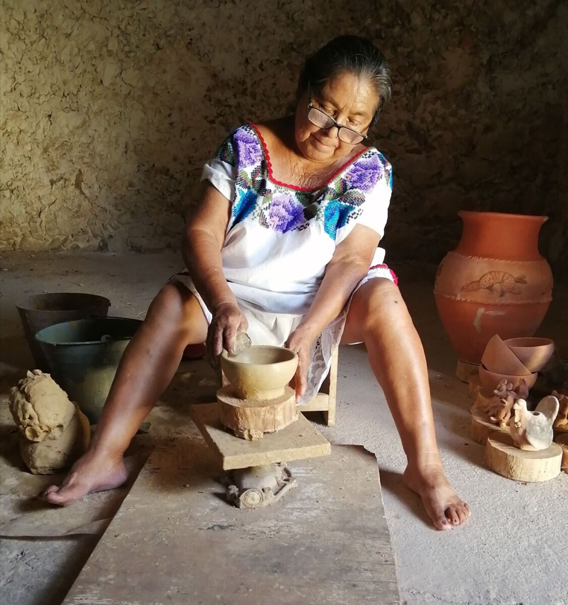 mujer artesana vestida con traje bordado trabajando una pieza de barro en el torno