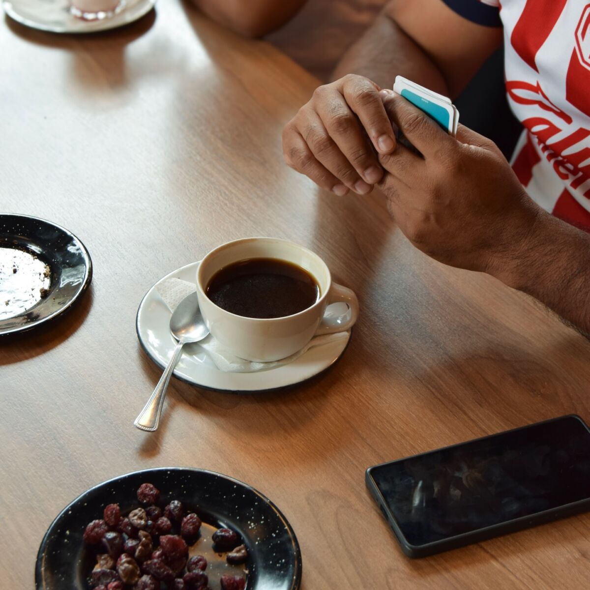 manos sosteniendo cartas de un juego de mesa, con un café americano y snacks en la mesa