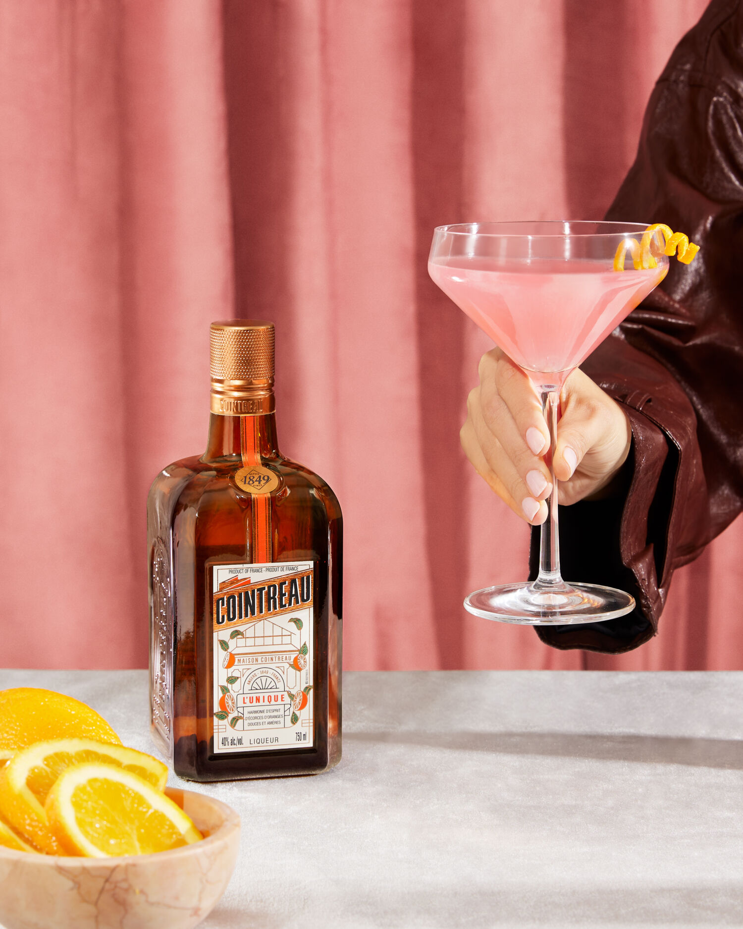 persona sosteniendo un coctel rosa junto a una botella de cointreau