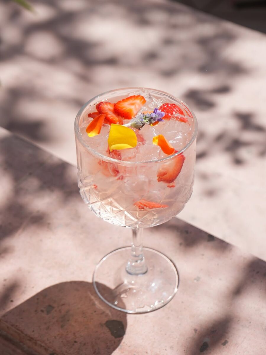 copa de cristal grande con un coctel cristalino con hielo y pétalos de rosa