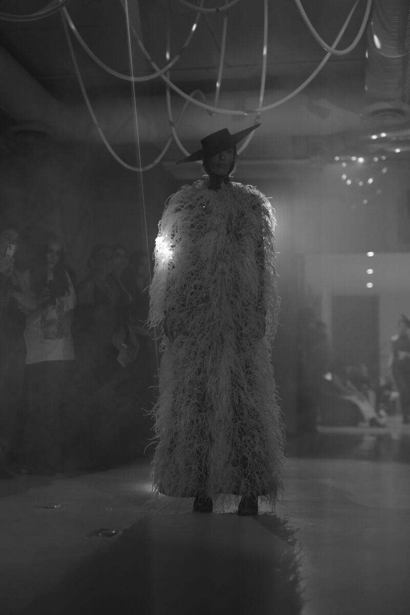 Persona con abrigo de plumas blanco y sombrero negro en una pasarela