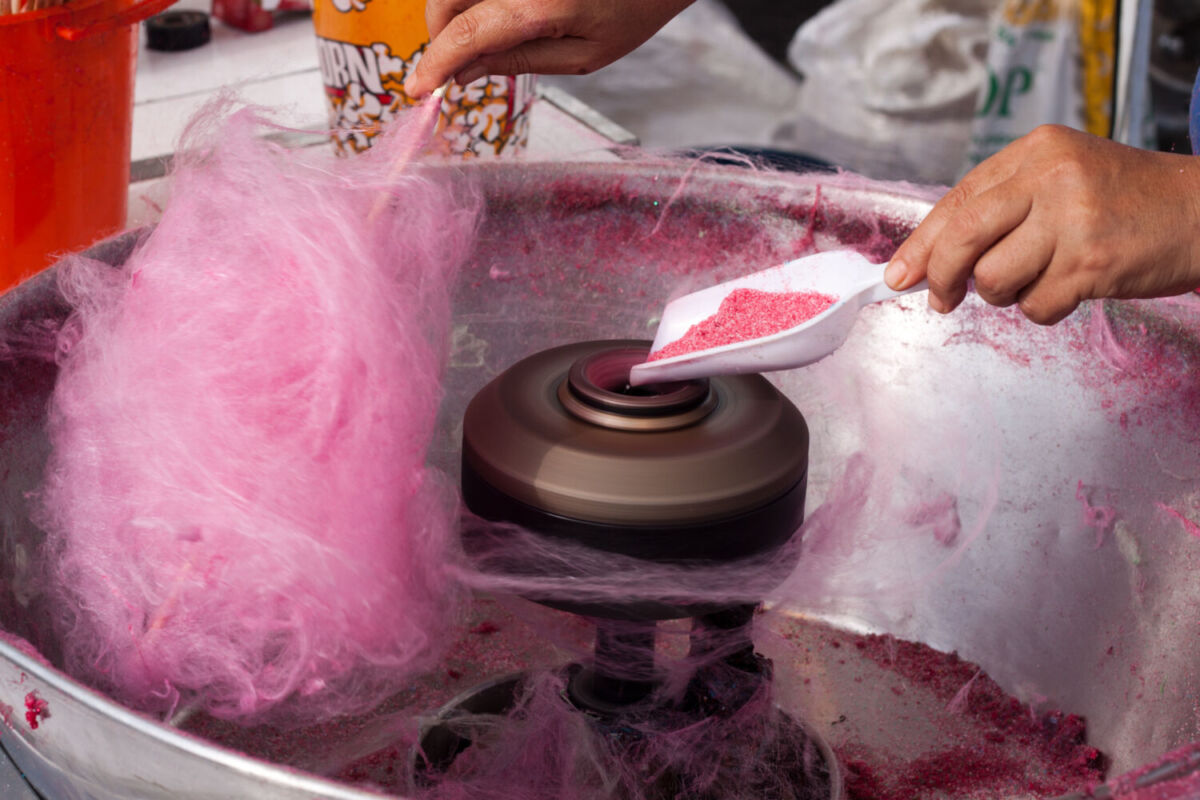 persona haciendo algodón de azúcar rosa en una máquina