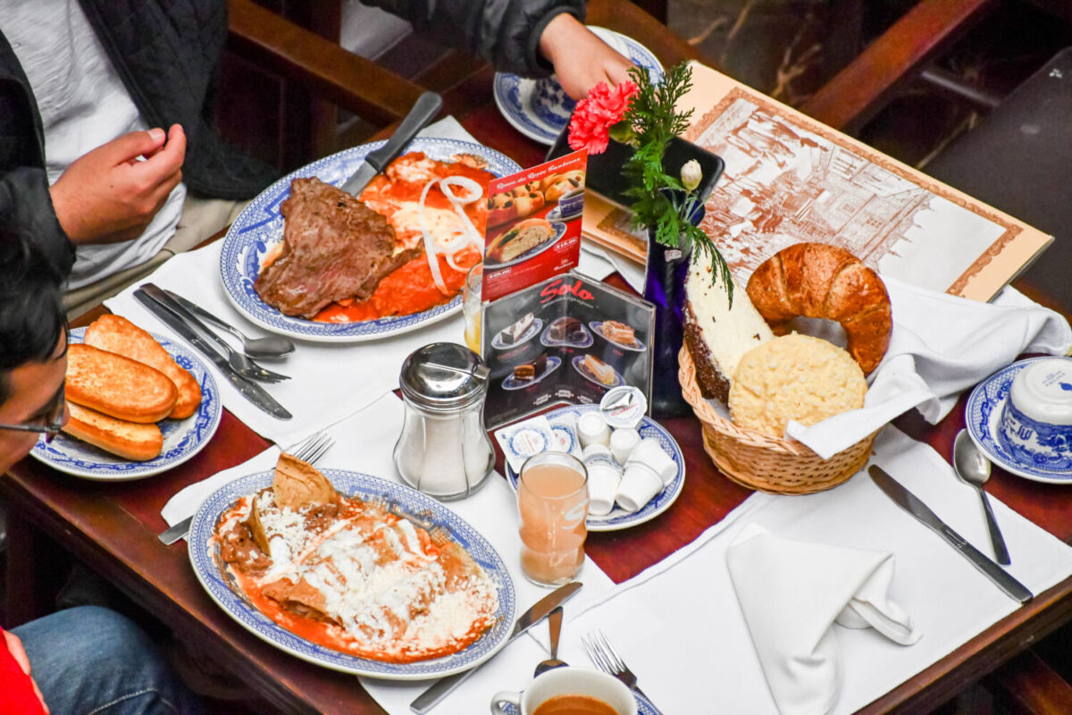 Desayuno típico Sanborns con enchiladas suizas, molletes y café en mesa con vajilla azul y blanca, Casa de los Azulejos CDMX.