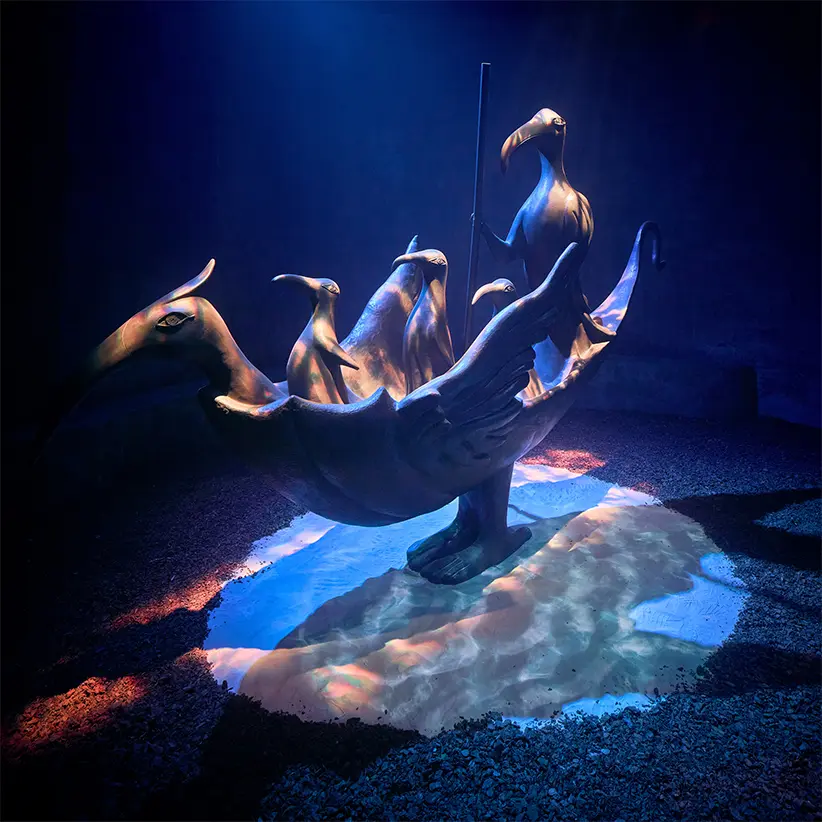 escultura de un barco con seres dentro de él bañado en luz 