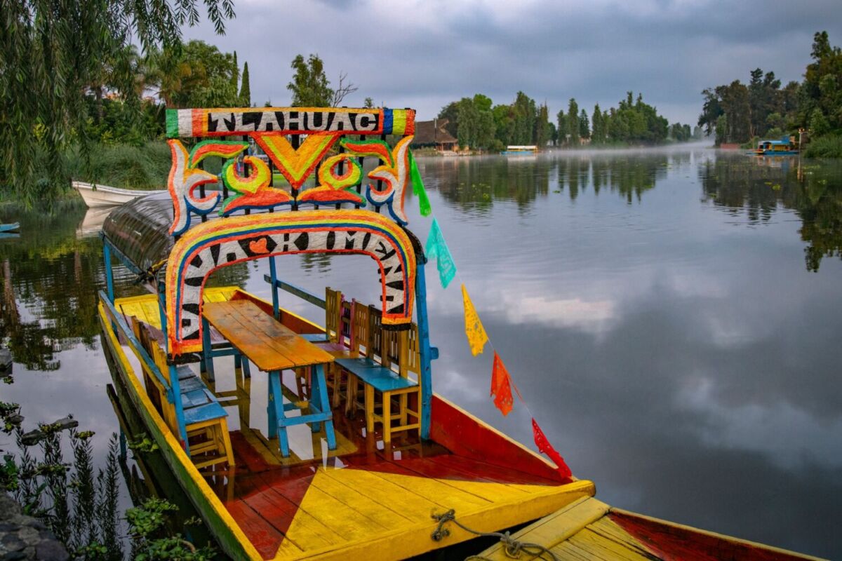 Trajinera colorida navegando por un canal estrecho rodeado de árboles de ahuejote en Tláhuac, Ciudad de Méxic